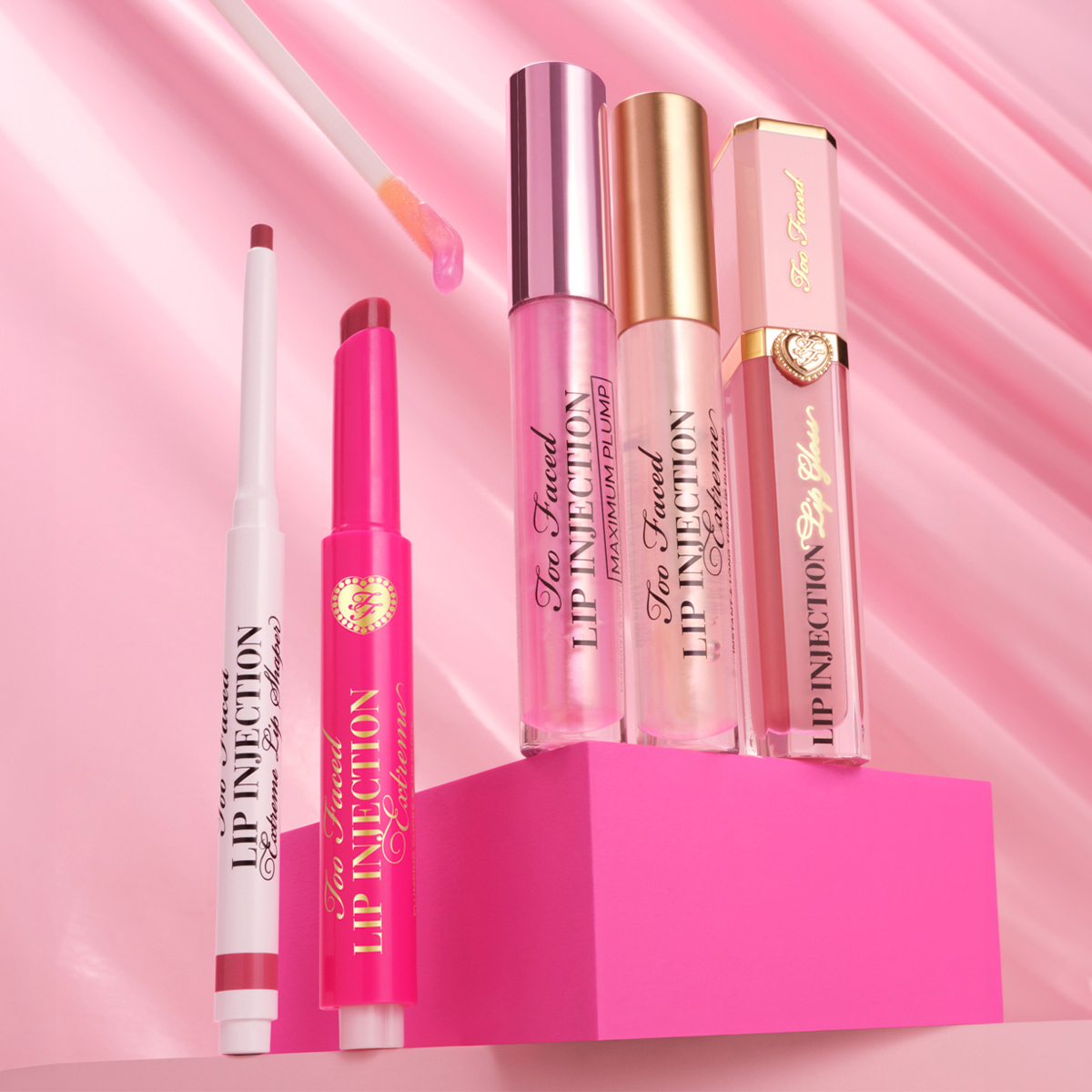Too Faced-leppeprodukter som står på en mørkerosa boks mot en lysrosa bakgrunn.
