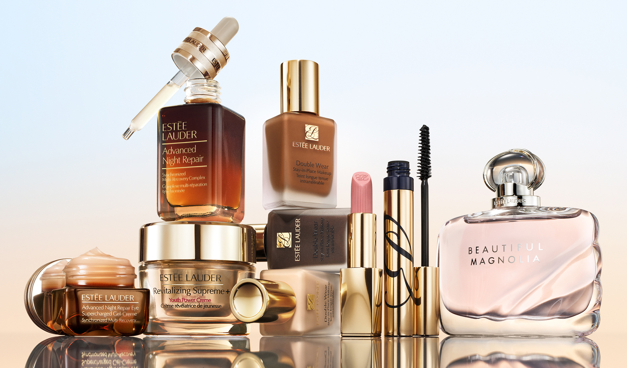 Estee Lauder -tuotteita, mukaan lukien seerumi, kosteusvoiteet, meikkivoide, huulipuna, ripsiväri ja hajuvesi, aseteltuna tyylikkäästi taustalla.