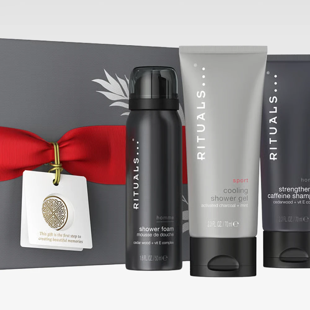 Bild som visar tre produkter från Rituals: en svart flaska med Rituals Homme Shower Foam, en grå tub med Rituals Sport Cooling Shower Gel, och en svart tub med Rituals Homme Strengthening Caffeine Shampoo. Bakgrunden är vit.