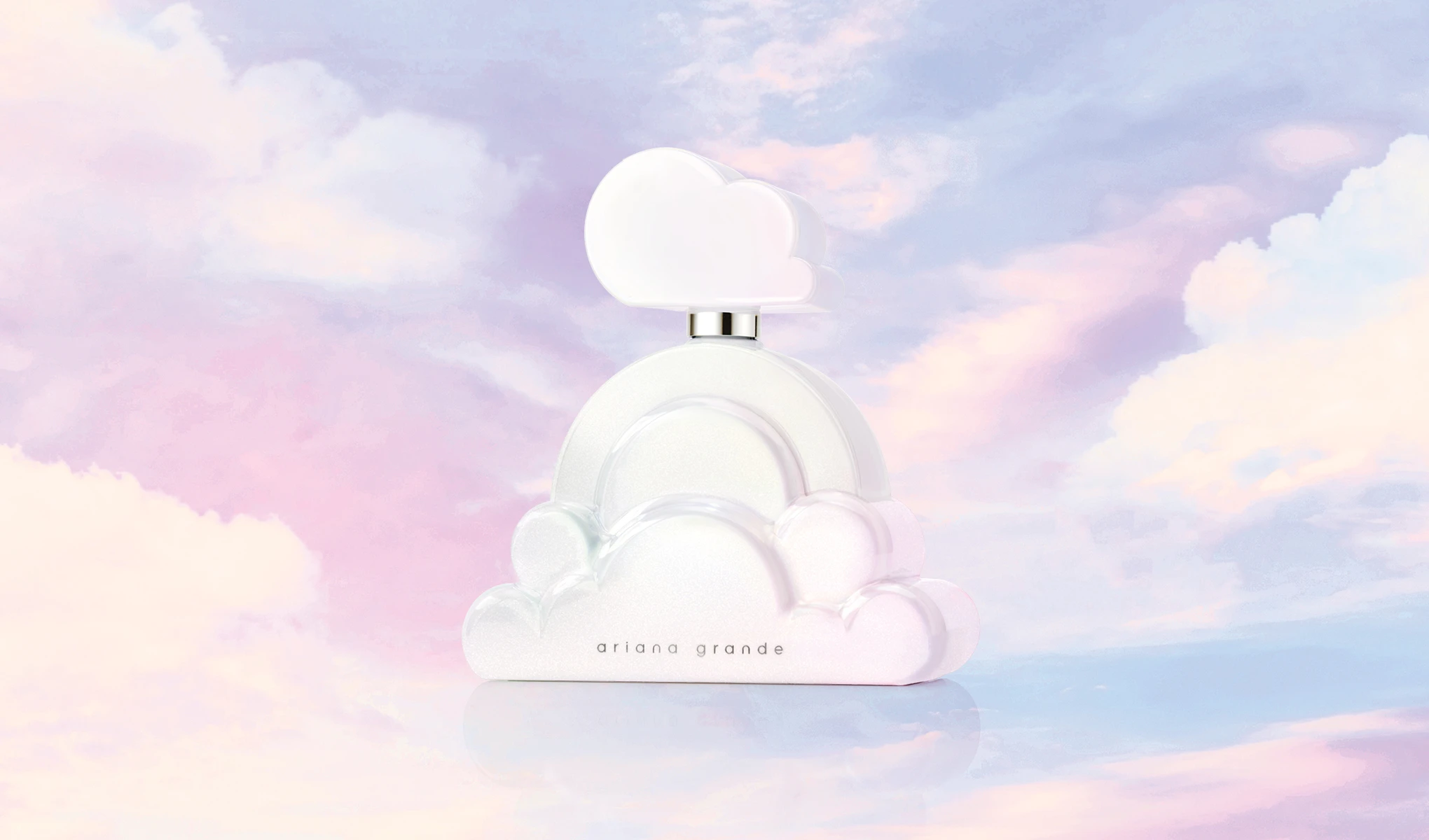 Hvit skyformet Ariana Grande parfymeflaske mot en pastellfarget himmelbakgrunn.