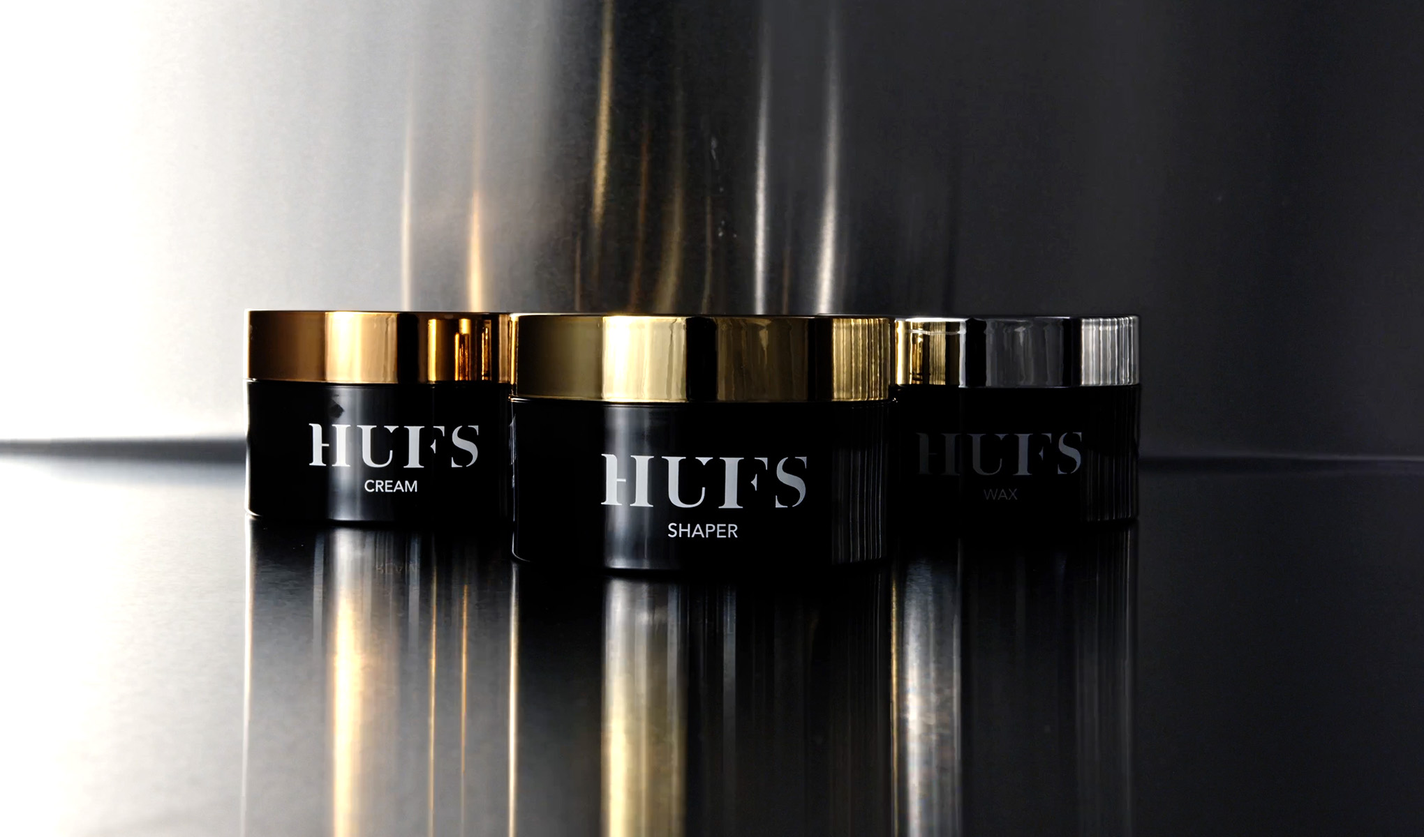 HUFS-produkter som kräm, shaper och vax i svarta burkar med guld- och silverlock.