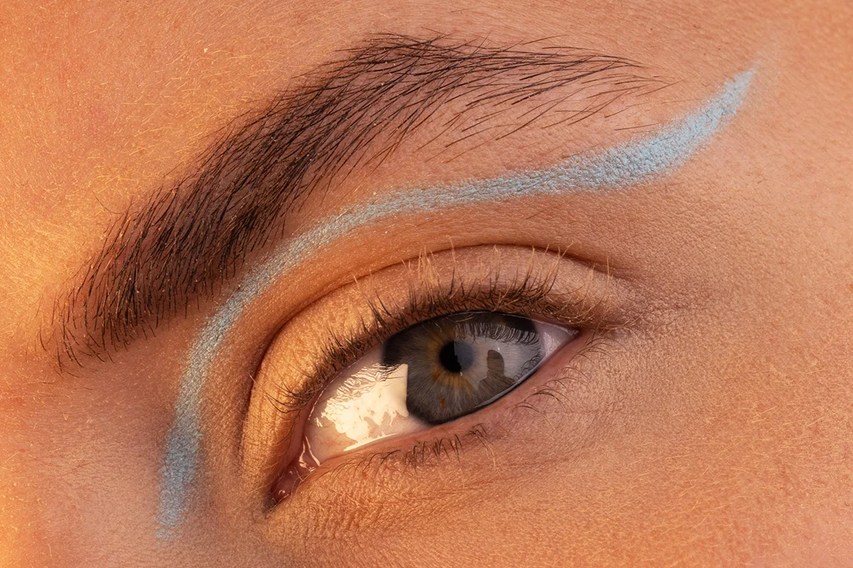 Närbild av ett öga med en kreativ blå eyeliner som sträcker sig ovanför ögonlocket och ögonbrynet
