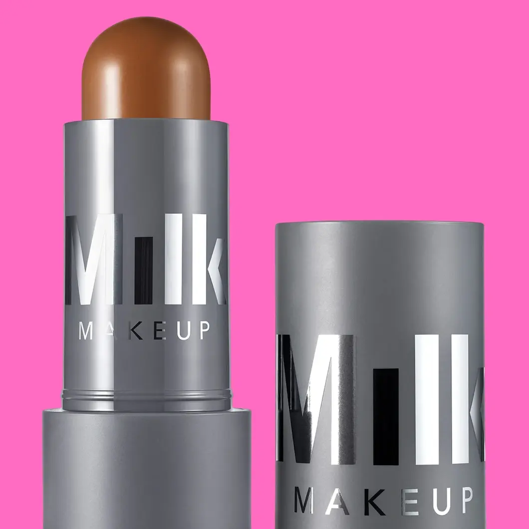 Milk Makeup bronzing stick, brun-bronse nyanse, i sølvfarget emballasje med hette, mot en rosa bakgrunn.