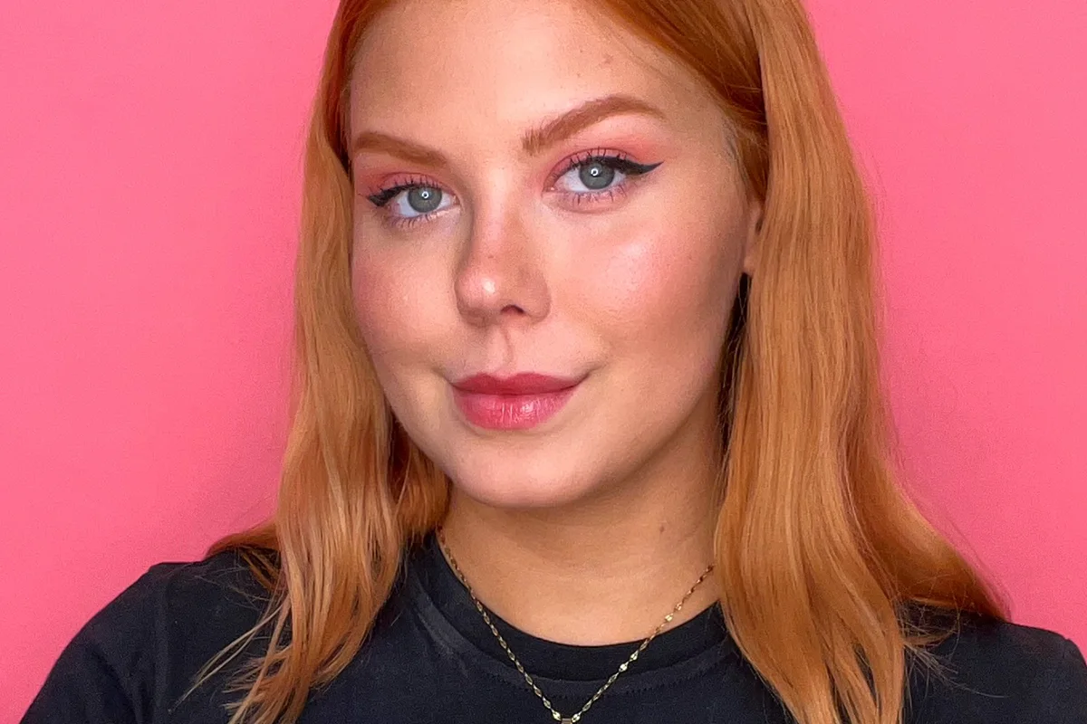 Närbild på en leende kvinna med rödblont hår och en färdig, naturlig sminkning med eyeliner, rouge och läppfärg