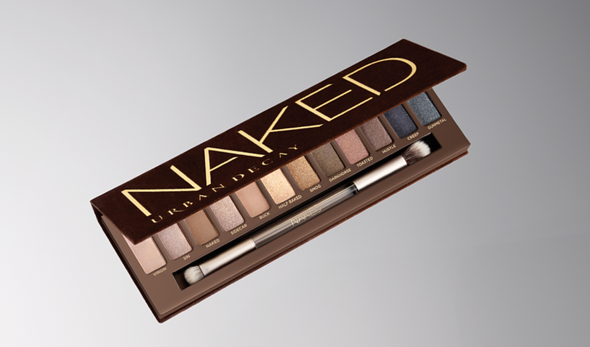 En ögonskuggspalett från Urban Decay med namnet "Naked" öppnad och placerad mot en grå bakgrund. Paletten innehåller olika nyanser av ögonskugga och en appliceringsborste.