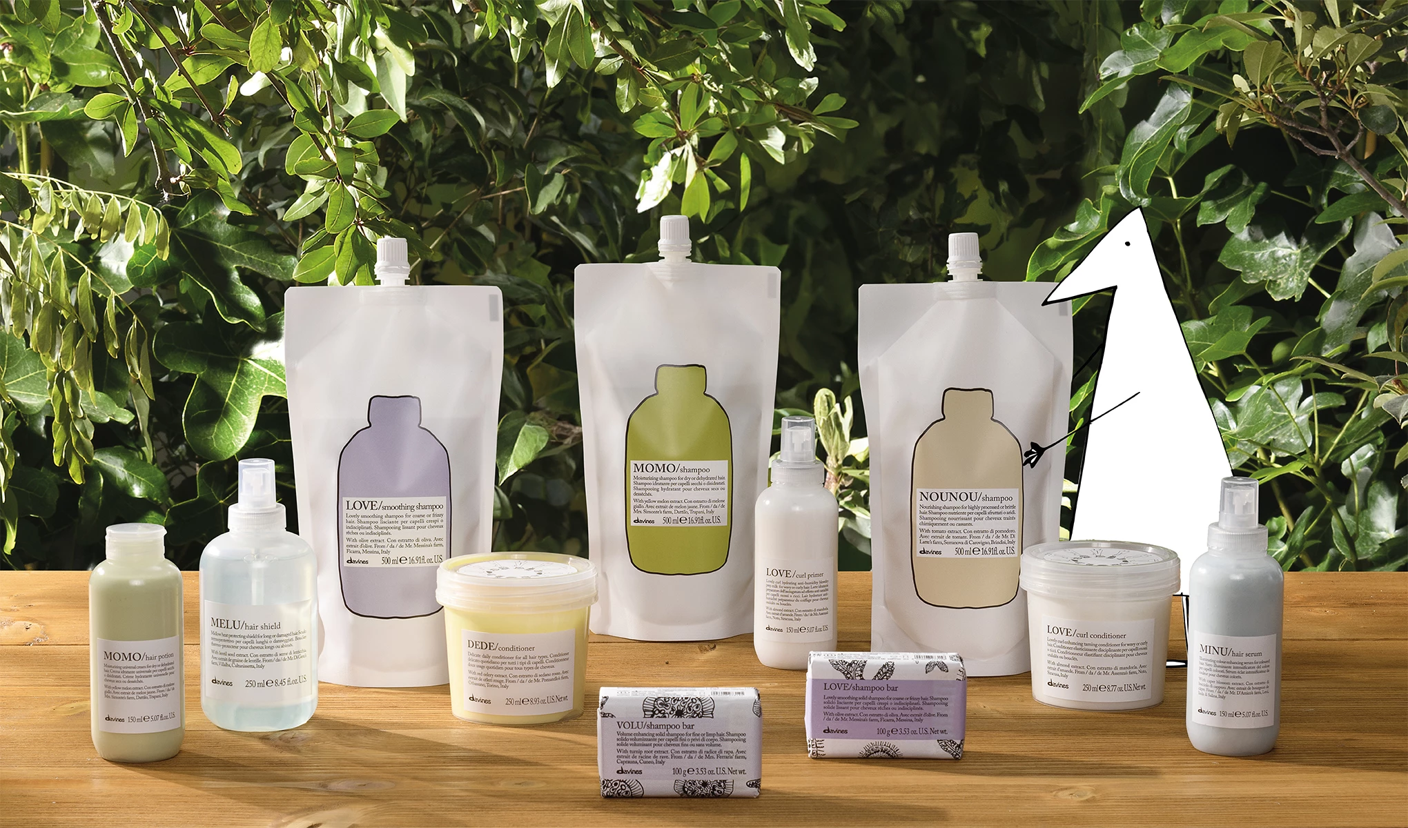En samling av Davines hårvårdsprodukter, inklusive schampo, balsam och stylingprodukter, placerade på ett träbord framför frodig grönska.