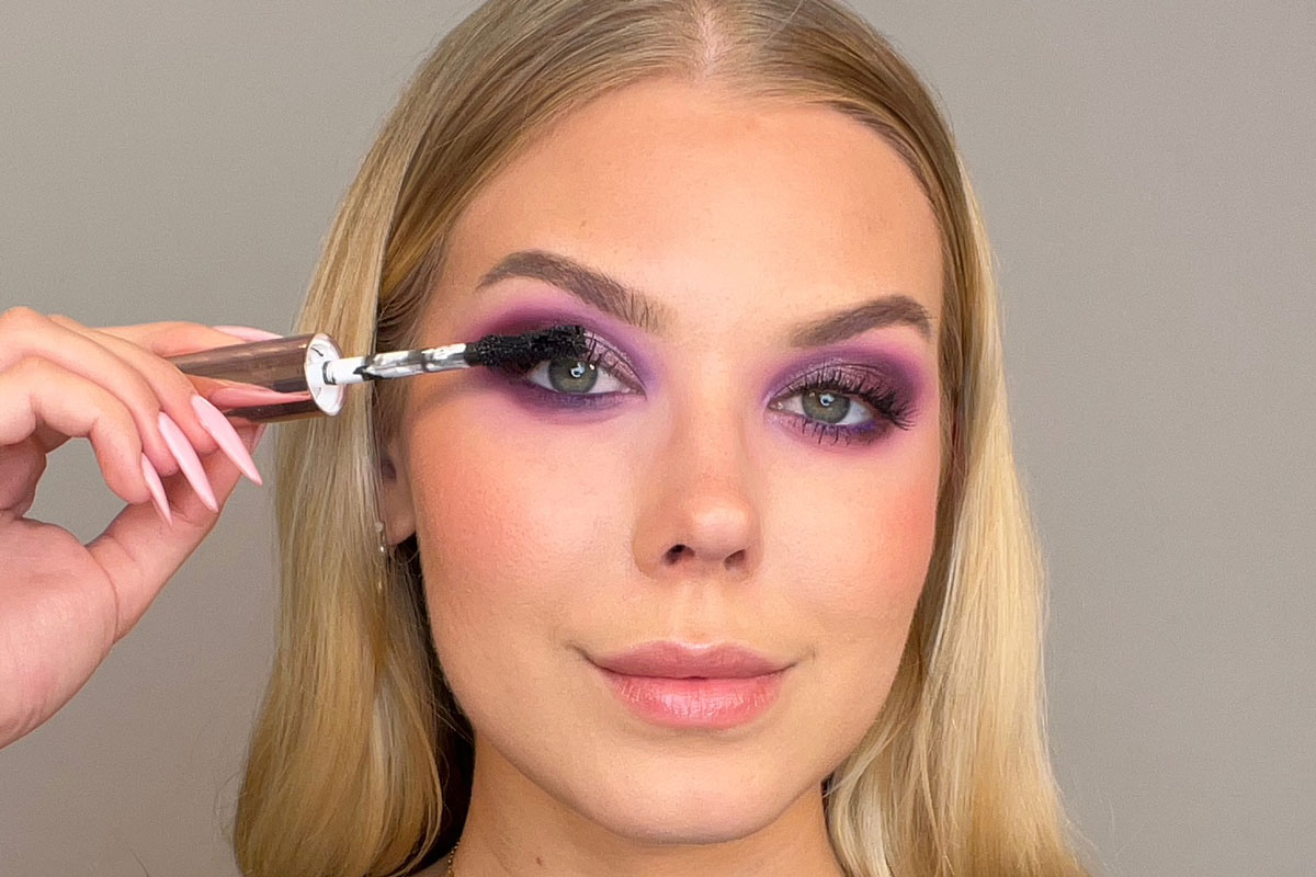 Kvinna med lila ögonmakeup som applicerar mascara.