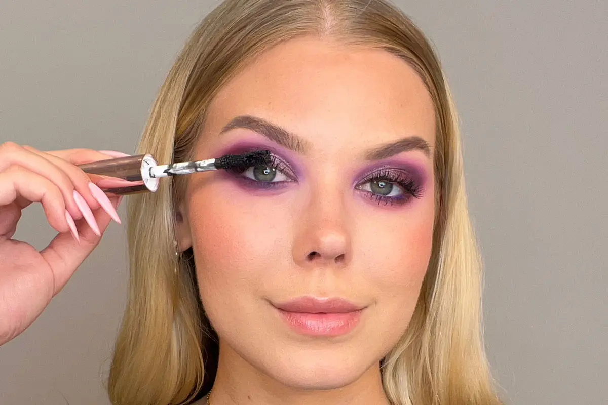 Kvinna med lila ögonmakeup som applicerar mascara.