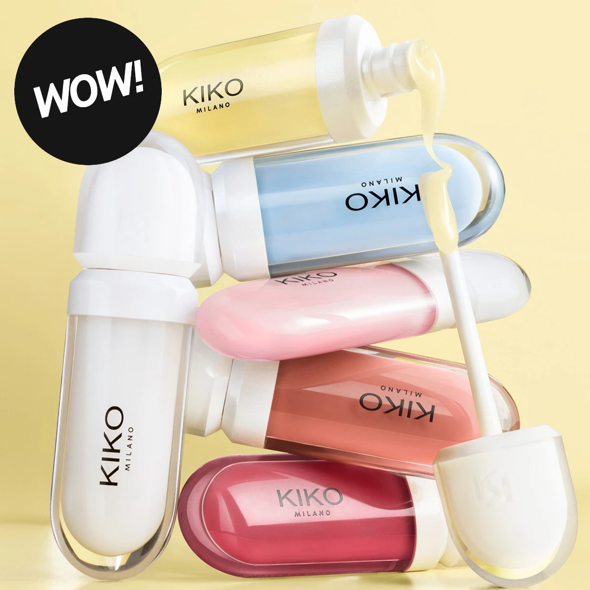 Flere KIKO MILANO-produkter i gjennomsiktige forpakninger med gult, blått, rosa, korallrødt og hvitt innhold mot en lysegul bakgrunn. En applikator med gult produkt vises sammen med en svart sirkel med den hvite teksten «WOW!».