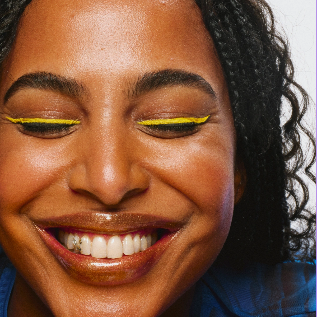 Närbild av ansikte med ögonmakeup: gul eyeliner längs fransraden, naturliga bryn och glansiga läppar.