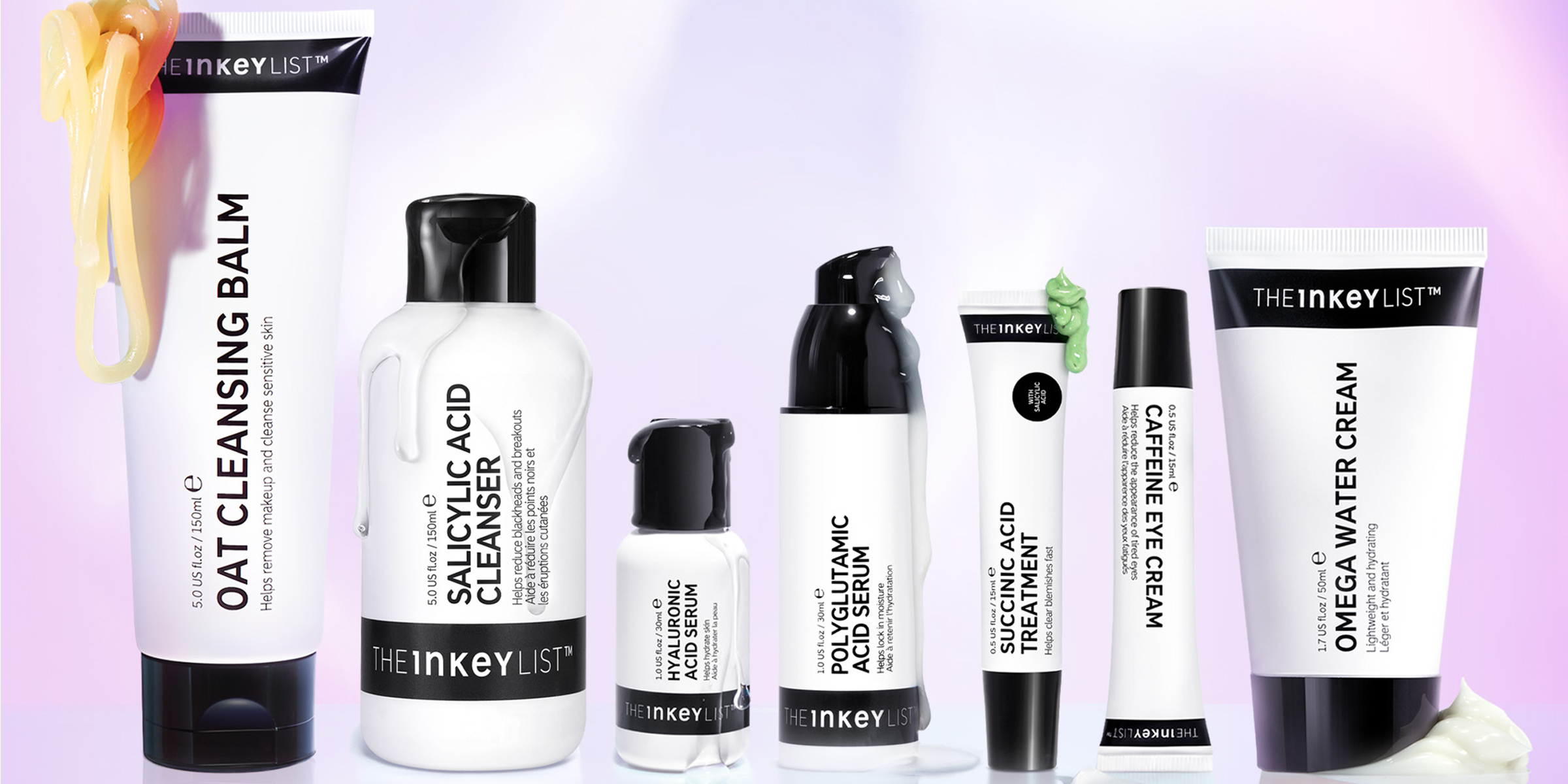 En samling hudpleieprodukter fra The Inkey List plassert på en lys flate mot en lyslilla bakgrunn. Ved siden av noen av produktene er det klemt ut krem. Emballasjen er hvit med svart tekst og detaljer.