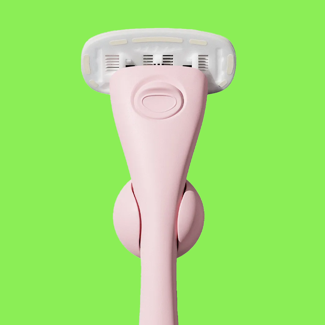 Barberhøvel i rosa design med flere blader mot grønn bakgrunn.