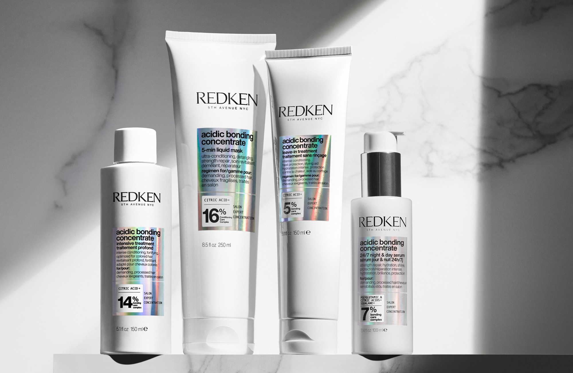 Neljä Redken Acidic Bonding Concentrate -hiustenhoitotuotetta valkoisissa pakkauksissa, aseteltuna vierekkäin vaaleaa marmoritaustaa vasten.