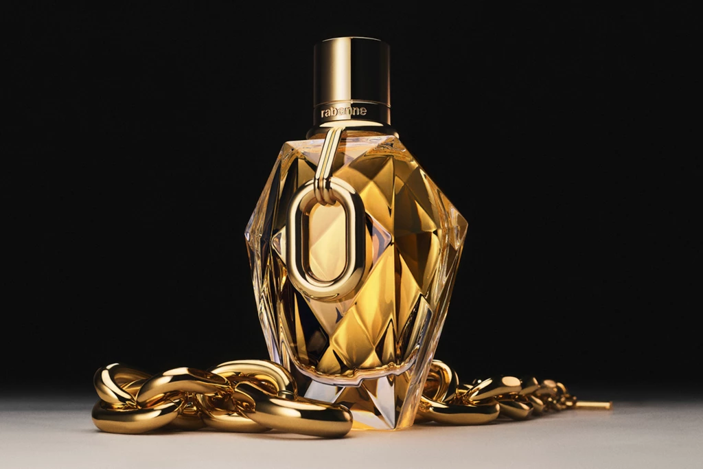 En parfymflaska från Paco Rabanne insvept i guldsmycken, placerad mot en mörk bakgrund