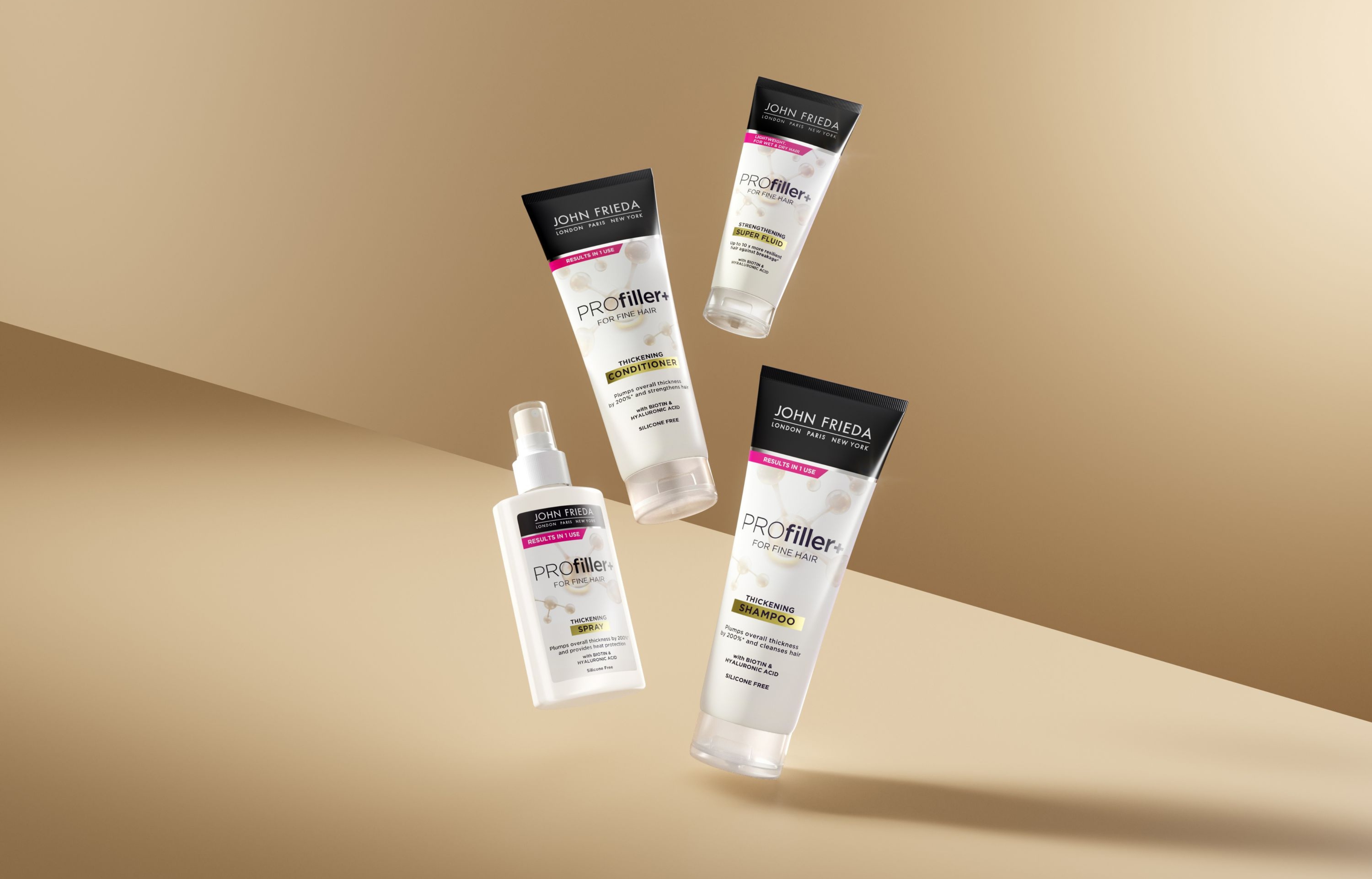 Neljä John Frieda Profiller+ -tuotetta vaaleanruskeaa taustaa vasten. Kuvassa on shampoo, hoitoaine, suihke ja hiusneste.