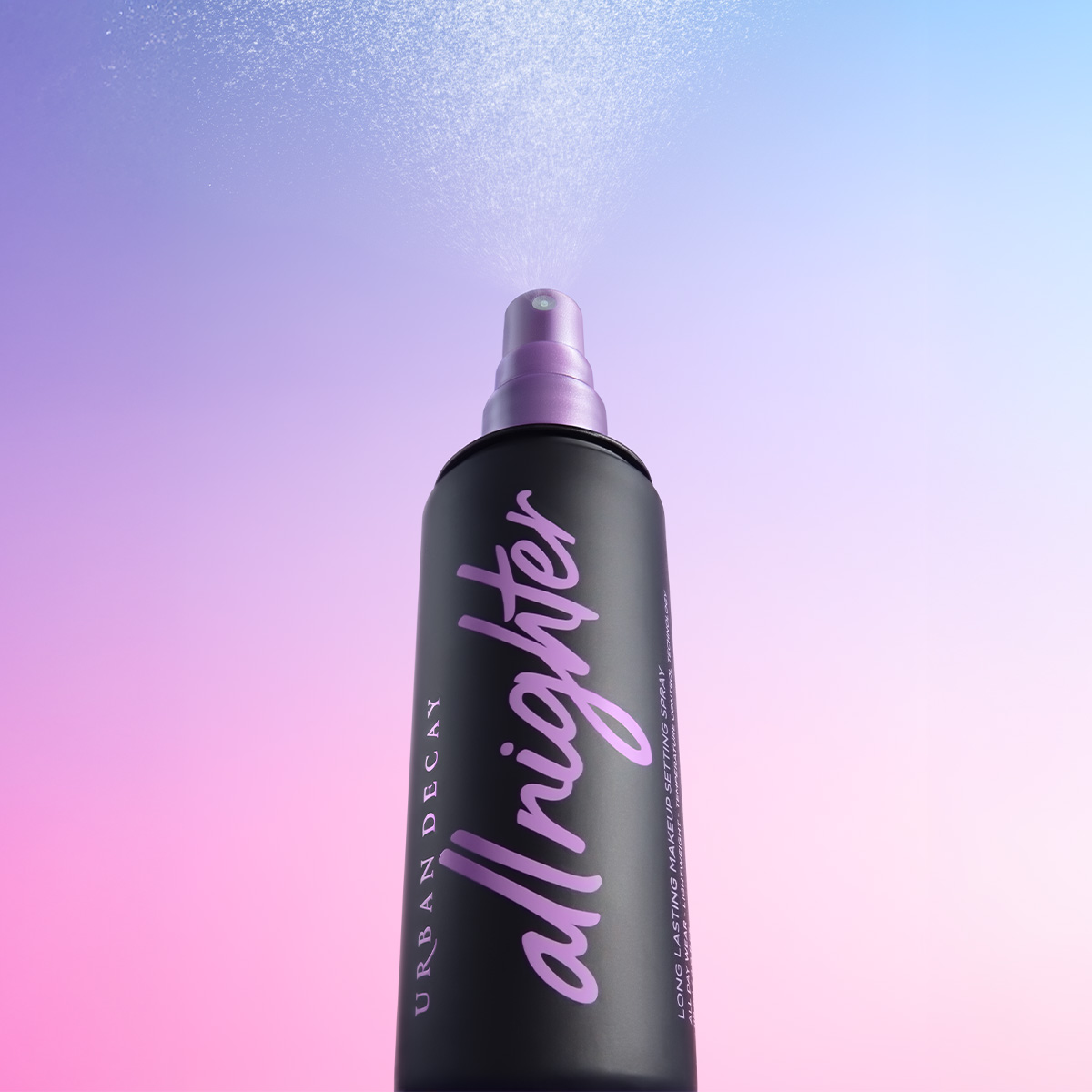 Musta suihkepullo, jossa on violetti teksti "all nighter" ja "URBAN DECAY", suihkuttaa sumua vaaleanpunaisella ja sinisellä liukuvärjätyllä taustalla.