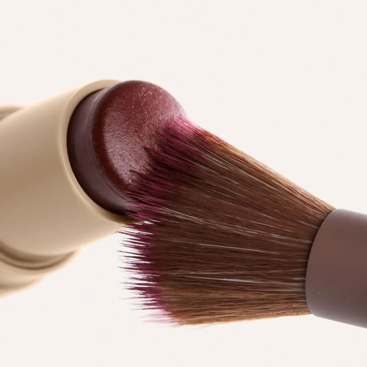 Nærbilde av en MIILD-blushstick og en sminkekost som påfører produktet.