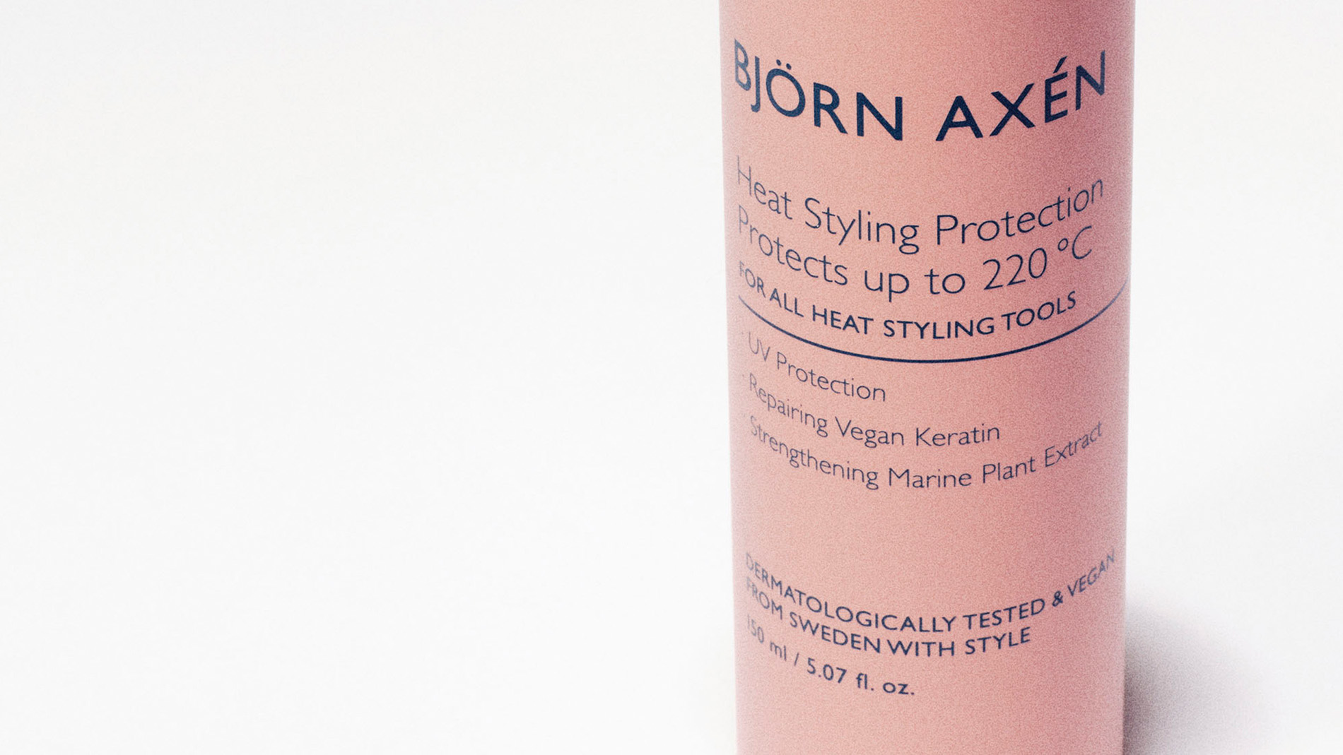 Vaaleanpunainen pullo, jossa lukee "BJÖRN AXÉN Heat Styling Protection" valkoista taustaa vasten.
