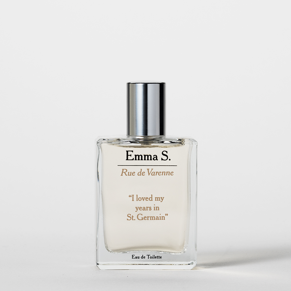 Läpinäkyvä Emma S -hajuvesipullo hopeanvärisellä korkilla, jossa tekstit “Rue de Varenne”, “I loved my years in St. Germain” ja “Eau de Toilette” vaaleaa taustaa vasten.