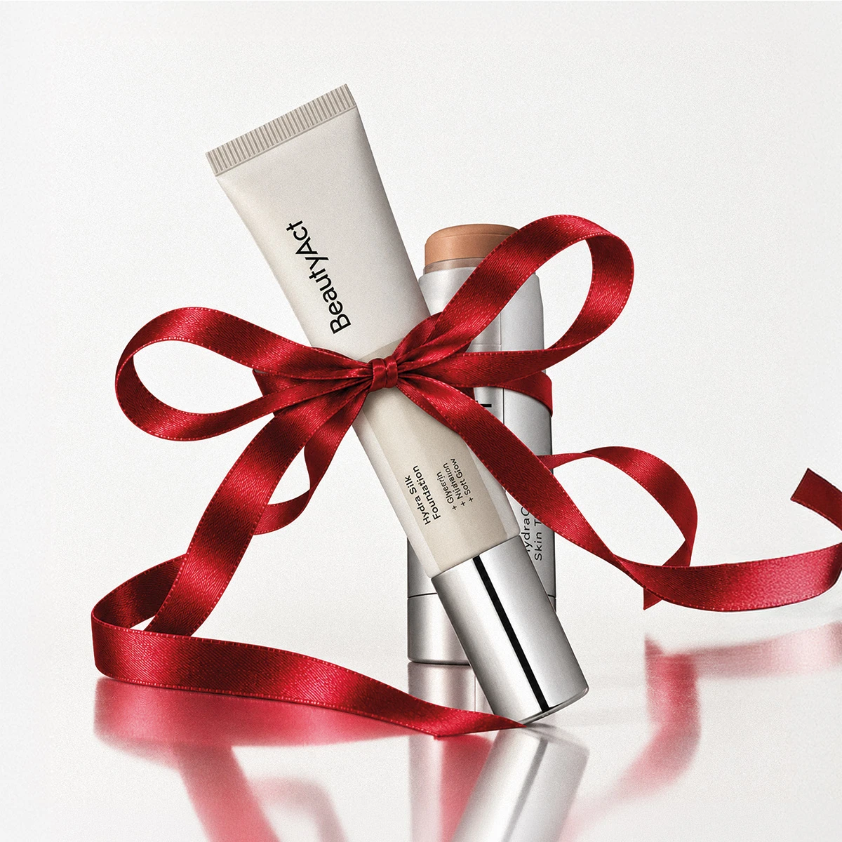 En BeautyAct Hydra Silk Foundation + Glycerin + Nuhuon + Soft Glow-tub och en annan produkt, inslagna med rött presentband.
