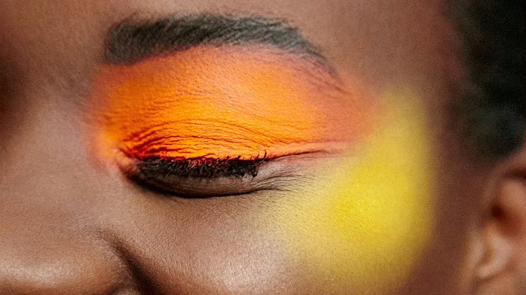 Närbild på en leende person med orange ögonskugga och gul rouge.