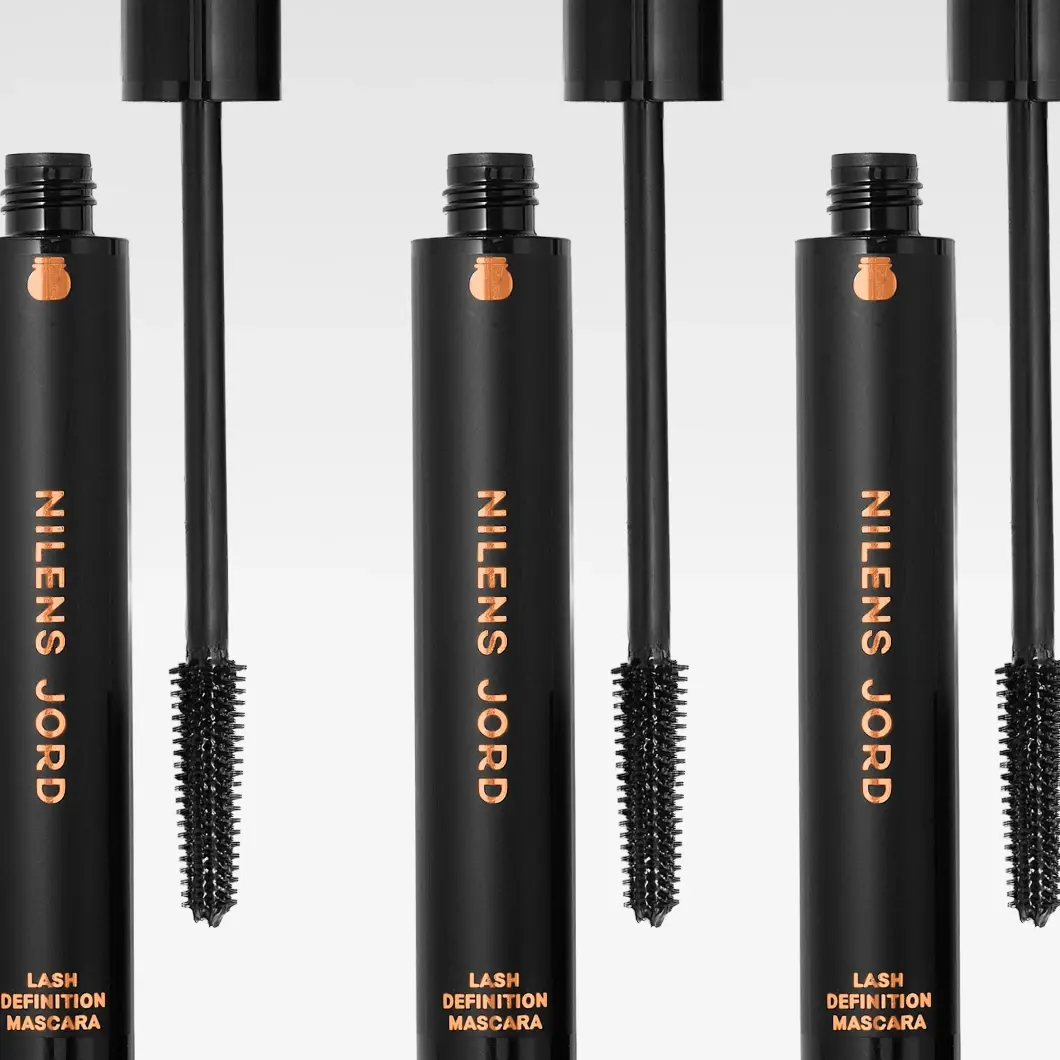 Flere svarte Nilens Jord Lash Definition Mascara med kobberfarget tekst og synlige mascarabørster.