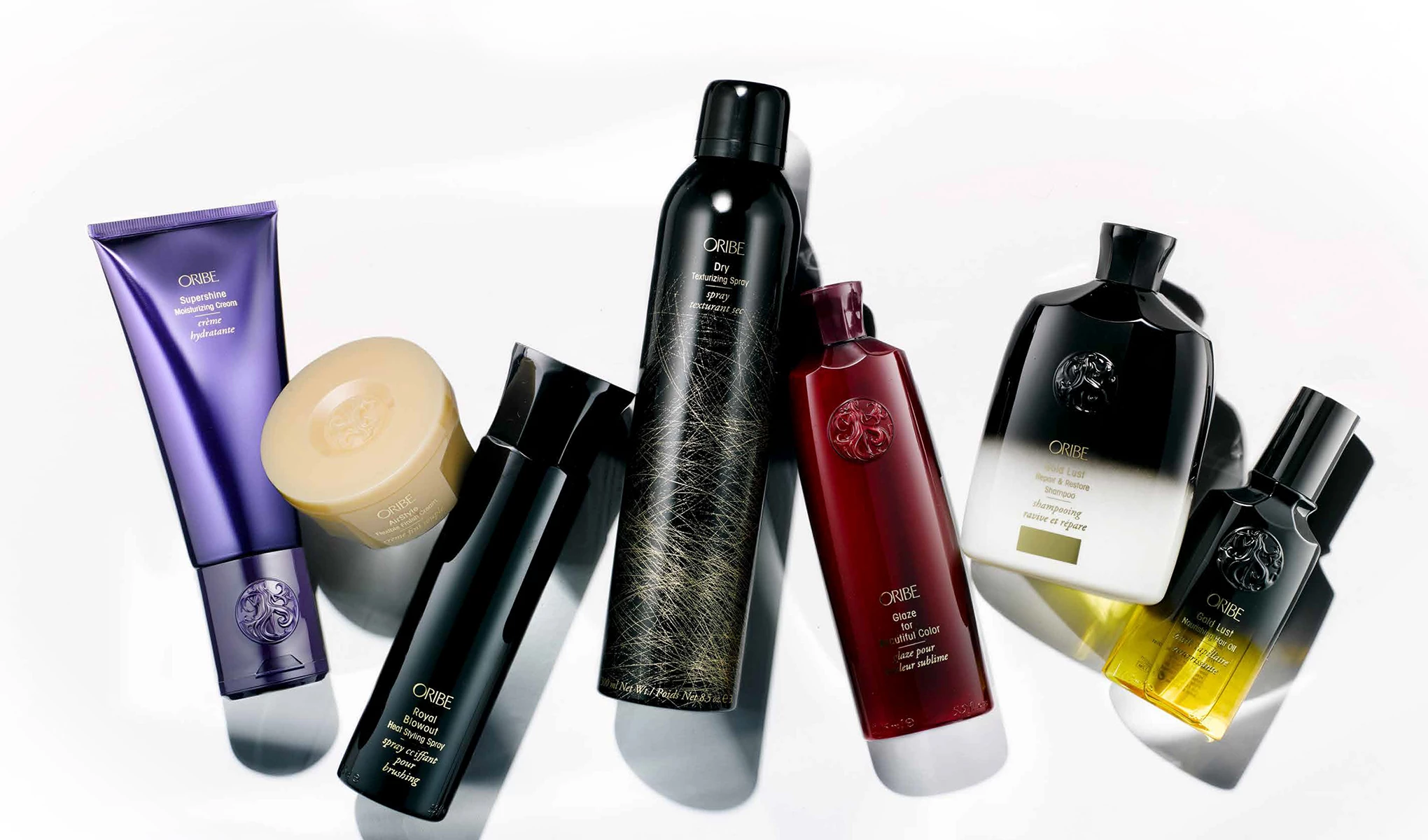 En samling hårvårdsprodukter från märket Oribe. Produkterna inkluderar en fuktgivande kräm i en lila tub, en hårmask i en rund behållare, en texturiserande spray i en svart flaska, en glansspray i en svart flaska, ett schampo i en svart och vit flaska, en glans för färgat hår i en röd flaska och en hårolja i en svart och gul flaska.