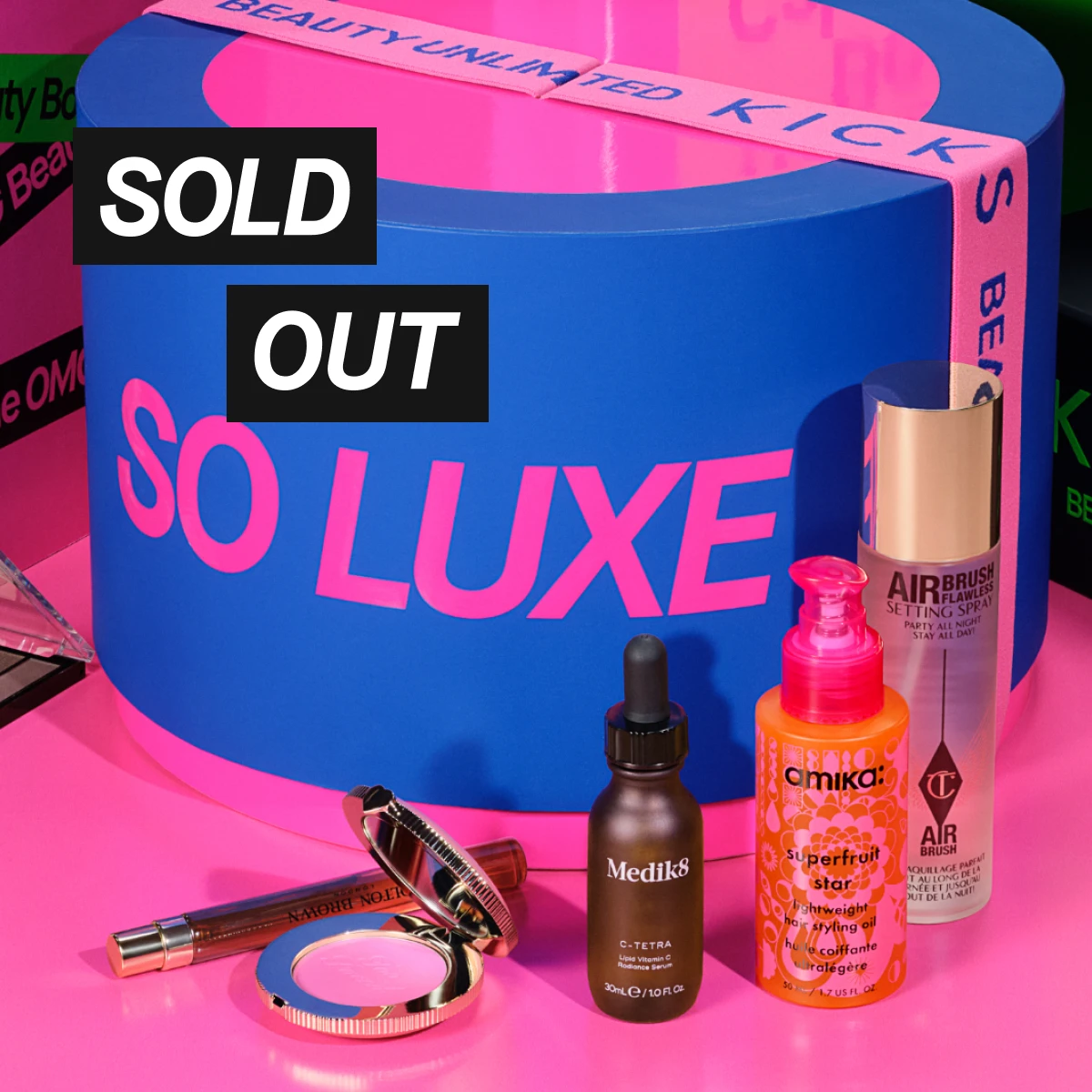 SOLD OUT. Blå och rosa SO LUXE-box med bandet “BEAUTY UNLIMITED KICKS”, tillsammans med Medik8 C-Tetra Lipid Vitamin C Radiance Serum 30 ml, amika Superfruit Star Lightweight Hair Styling Oil, Charlotte Tilbury Airbrush Flawless Setting Spray och makeup.