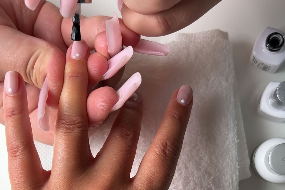 En klar topplack appliceras för att försegla nagelkonstdesignen med vita prickar.