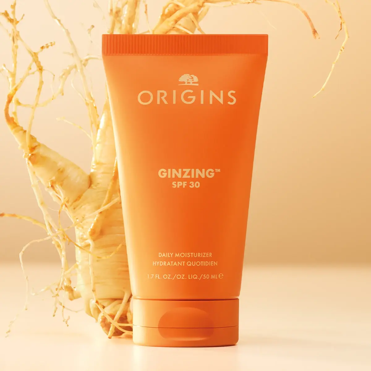 Origins GinZing SPF 30 Daily Moisturizer står foran en ginseng-rot mot en lysoransj bakgrunn.