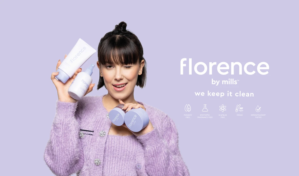 Violettiin neuletakkiin pukeutunut henkilö pitää kädessään useita Florence by Mills -merkin ihonhoitotuotteita. Tausta on vaalean violetti ja teksti ”florence by mills we keep it clean” on sijoitettu henkilön oikealle puolelle. Tekstin alapuolella on kuvakkeita, jotka osoittavat, että tuotteet eivät sisällä parabeeneja, synteettisiä hajusteita, SLS/SLES:ää, ovat vegaanisia ja dermatologisesti testattuja.