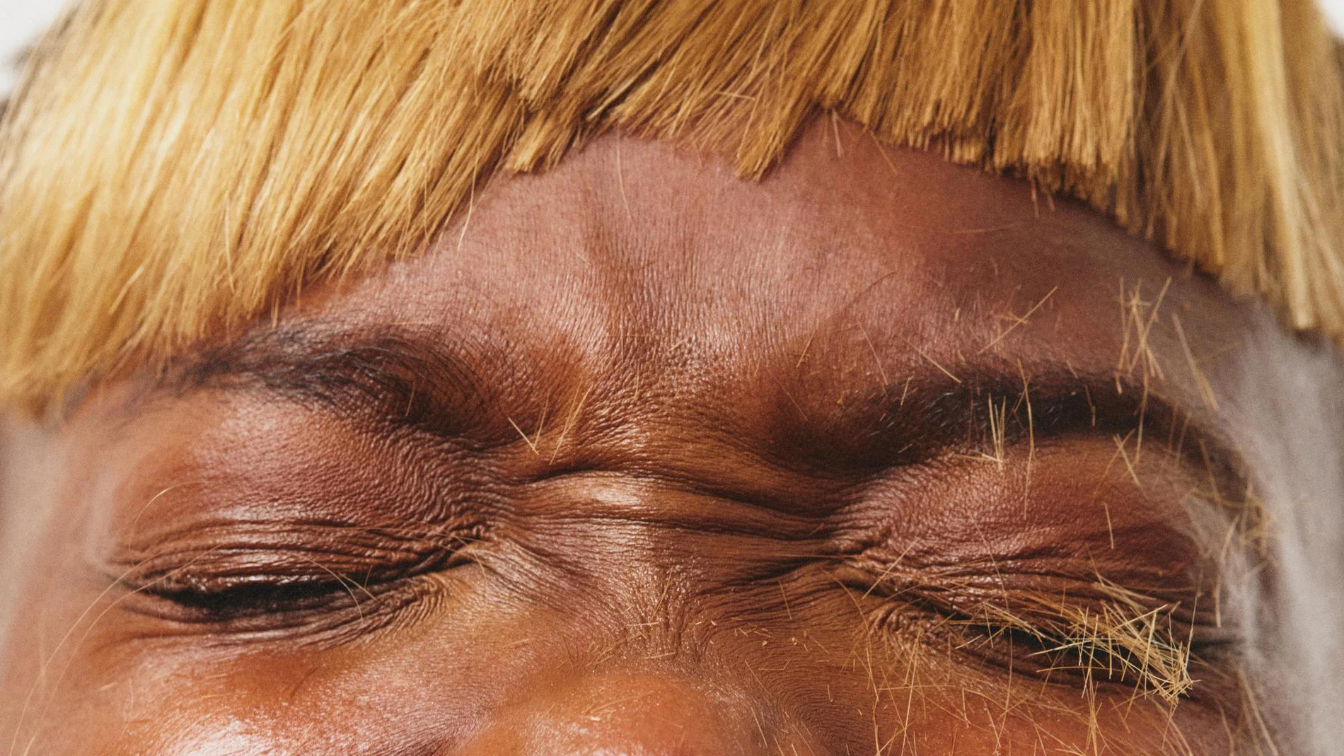 Nærbilde av et ansikt med lukkede øyne og rynket panne. Personen har en lys blond, rettklippet lugg og avklippede hårstrå liggende på øyelokkene.