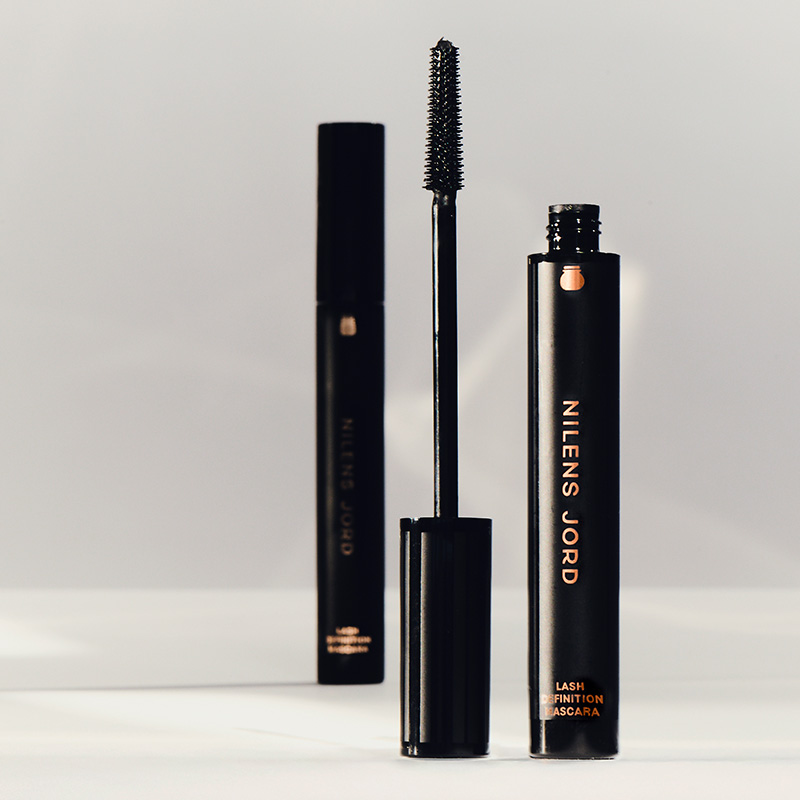 Nilens Jord Lash Definition Mascara. To svarte mascara-tuber, den ene med børsten ute og den andre lukket. Tubene har gullfarget tekst.