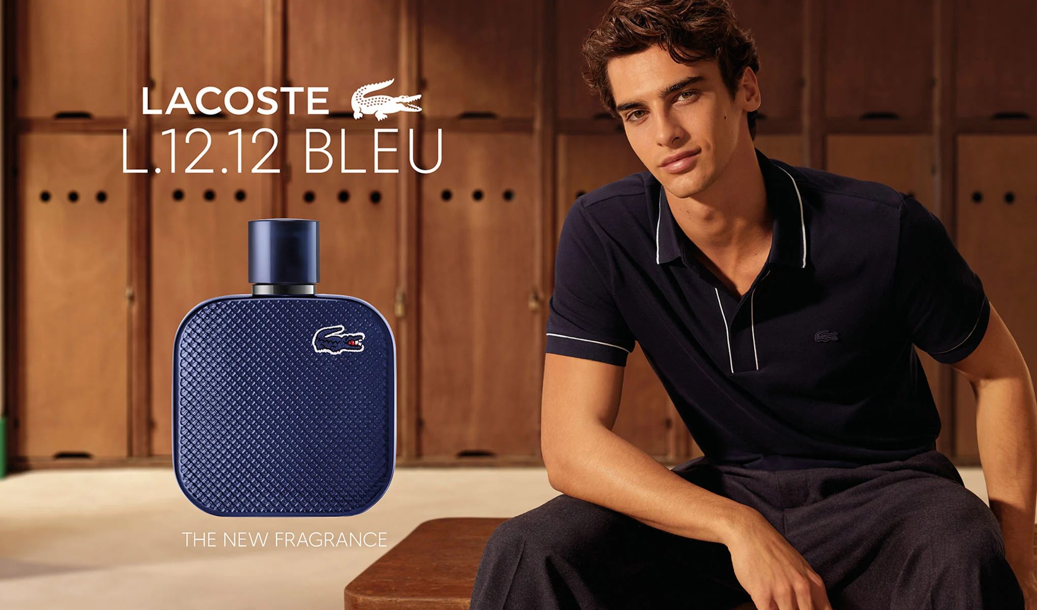 Lacoste L.12.12 Bleu-parfymflaska och en sittande man i omklädningsrumsmiljö. Bilden innehåller texterna ”Lacoste L.12.12 Bleu” och ”The New Fragrance”.