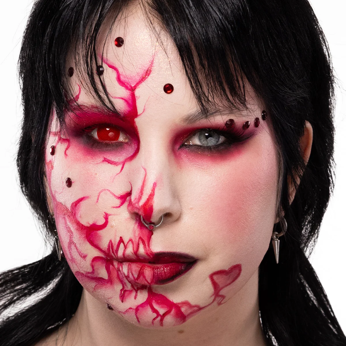 Närbild av en person med mörkt hår, klädd i svart. Personen har en kreativ sminkning med mörka och dramatiska ögon.