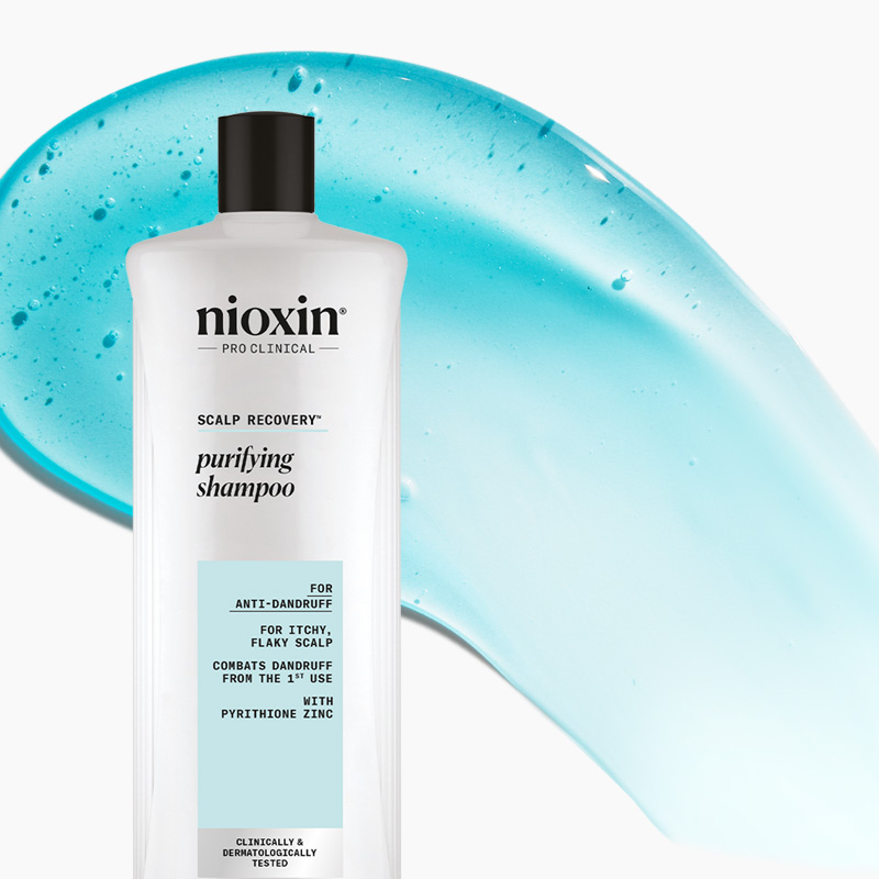 Nioxin Pro Clinical puhdistava hilse-shampoo valkoisessa pullossa, jossa on musta korkki, sinistä taustaa vasten.