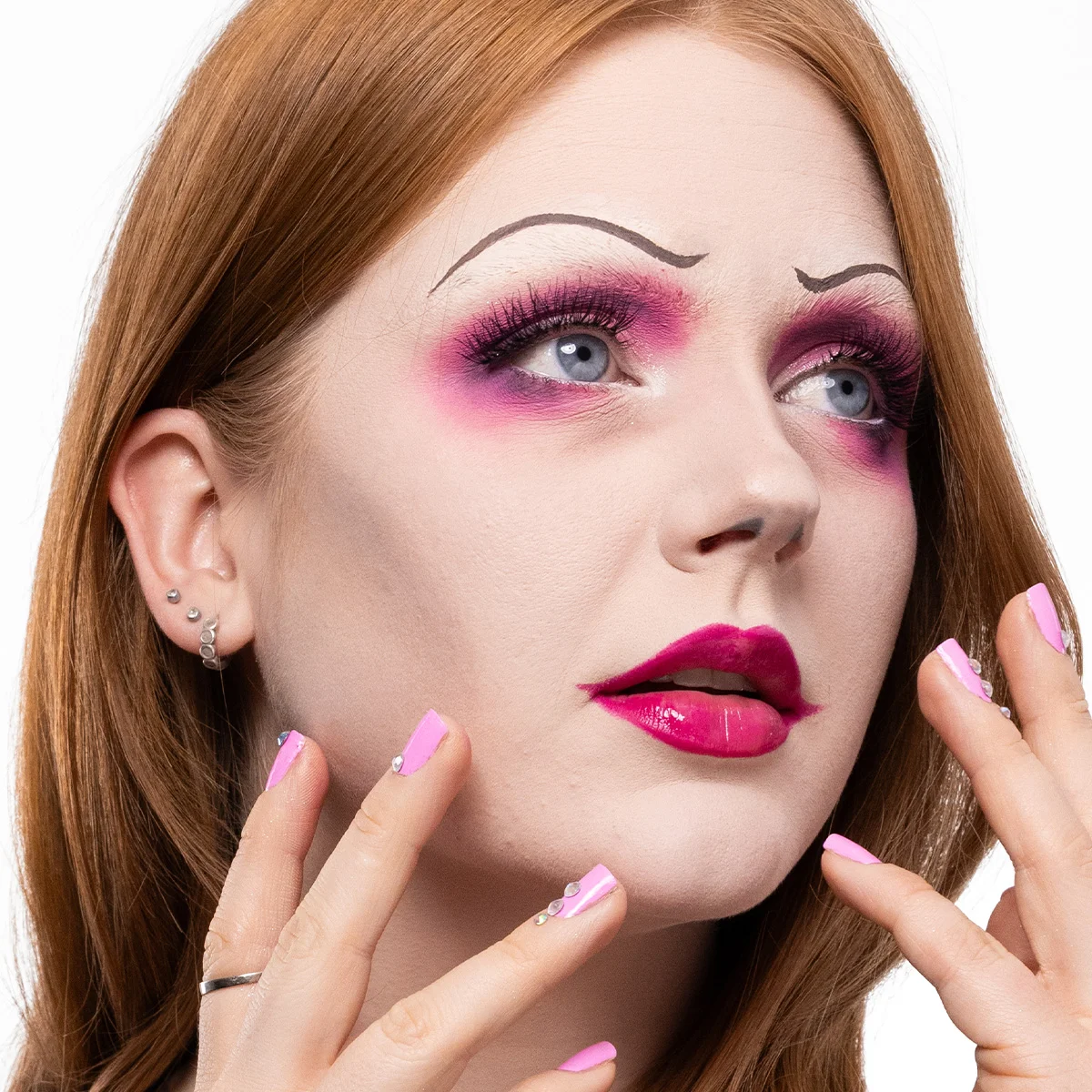 Närbild av en person med rött hår och rosa naglar. Personen har flera örhängen i vänstra örat och håller i sitt hår.