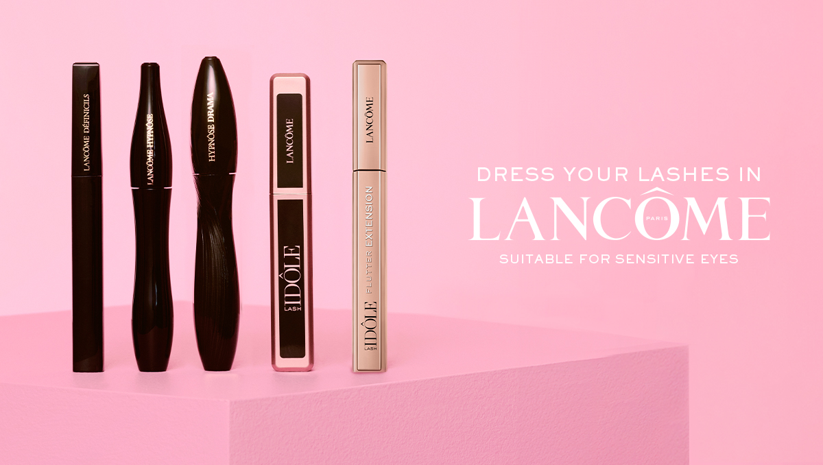 Fem Lancôme mascara-produkter står uppradade på ett rosa podium mot en rosa bakgrund, inklusive Définicils, Monsieur Big, Hypnôse Drama och Lash Idôle Flutter Extension. Texten “DRESS YOUR LASHES IN LANCÔME PARIS” och “SUITABLE FOR SENSITIVE EYES” visas bredvid produkterna.