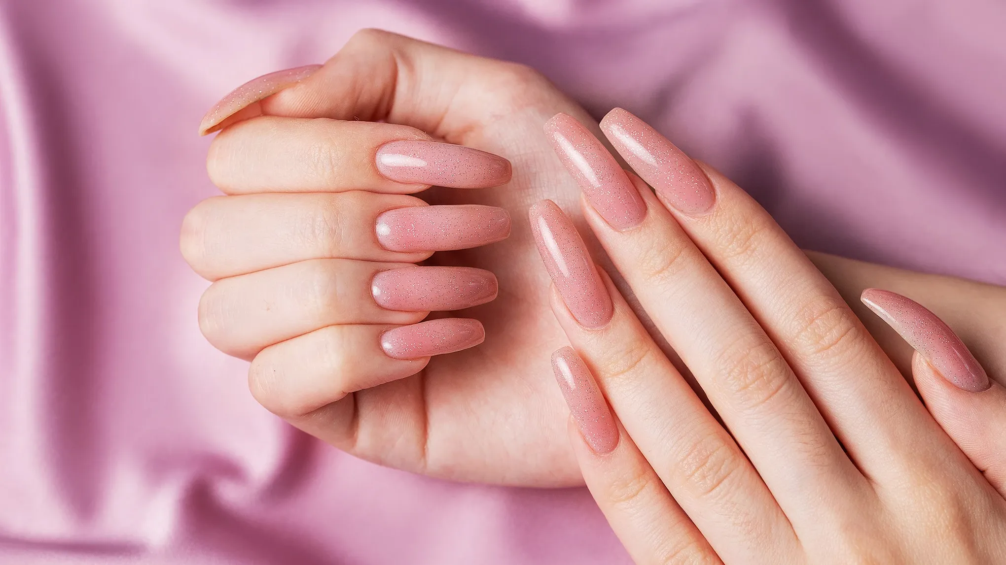 To hender med rosa løsvnegler mot en rosa bakgrunn av silke