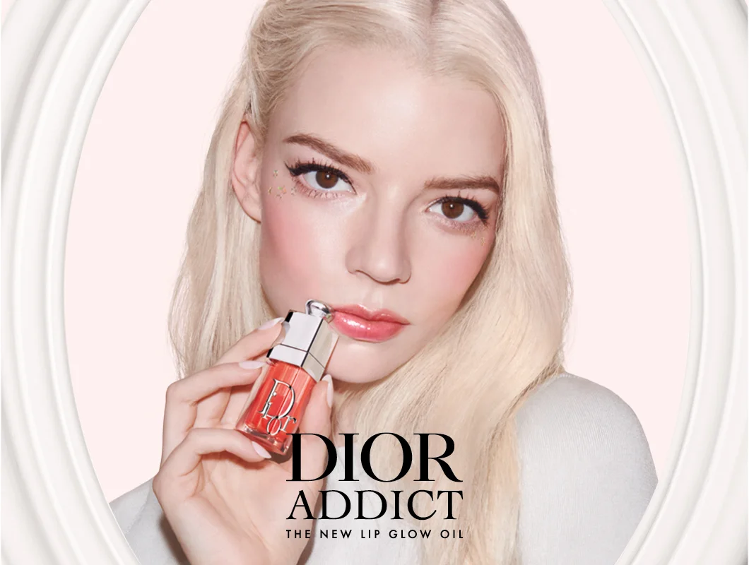 Ljus­hårig kvinna håller Dior Addict Lip Glow Oil nära läpparna mot en ljusrosa bakgrund.