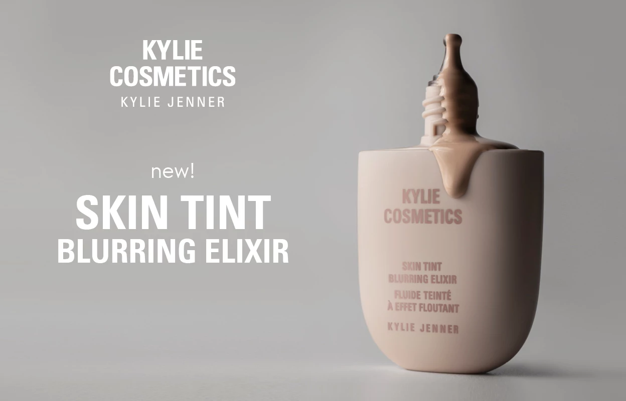 Brun, rinnandes flaska Skin tint av Kylie Cosmetics, tillsammans med Loggan och texten "new! SKIN TINT BLURRING ELIXIR" i vitt mot en grå bakgrund