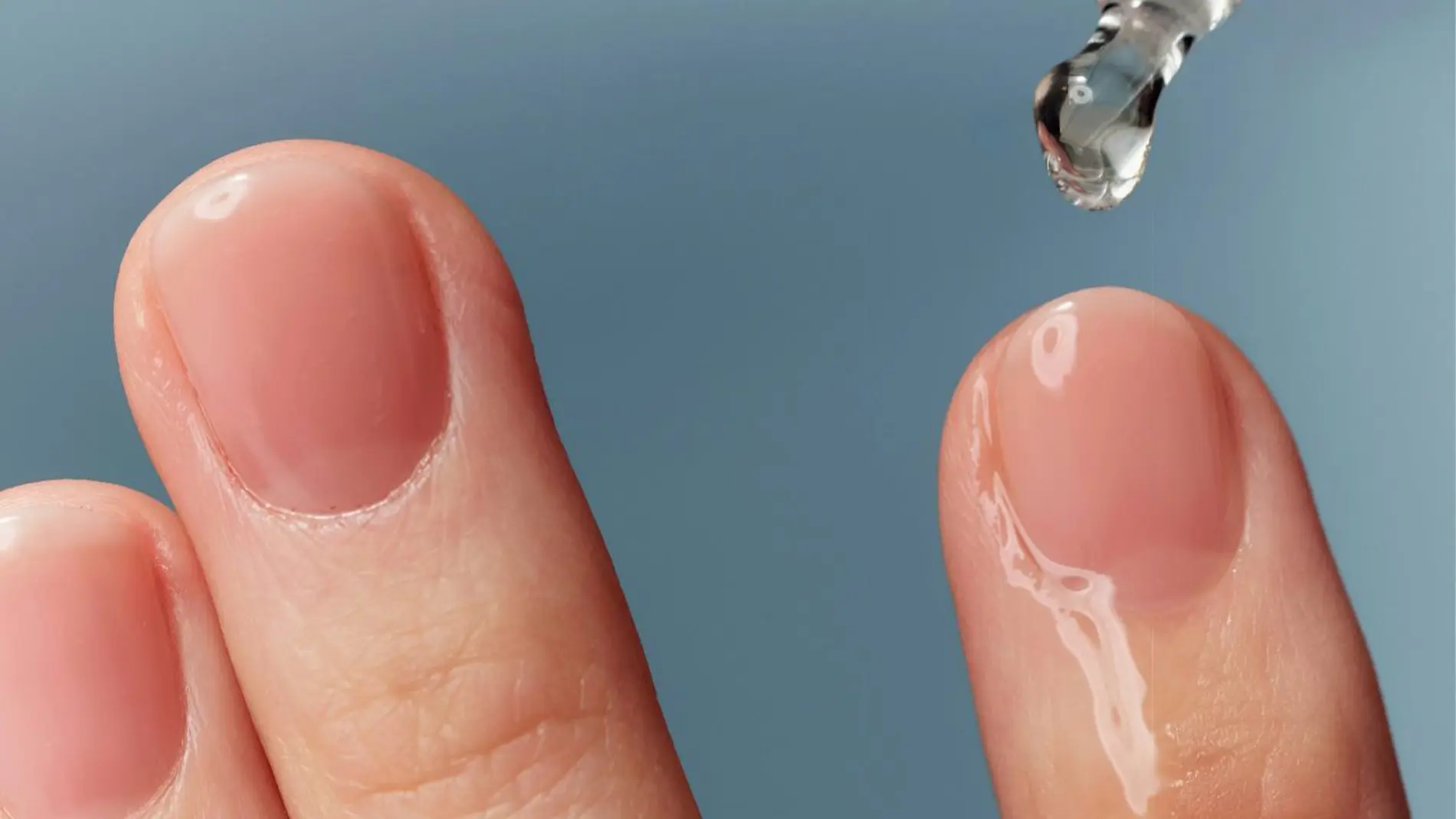 Lähikuva sormista, joille levitetään läpinäkyvää ihonhoitoseerumia pipetillä vaaleansinistä taustaa vasten. Kosteuttava skincare-seerumi korostuu kiiltävällä pinnalla ja minimalistisella beauty-ilmeellä.