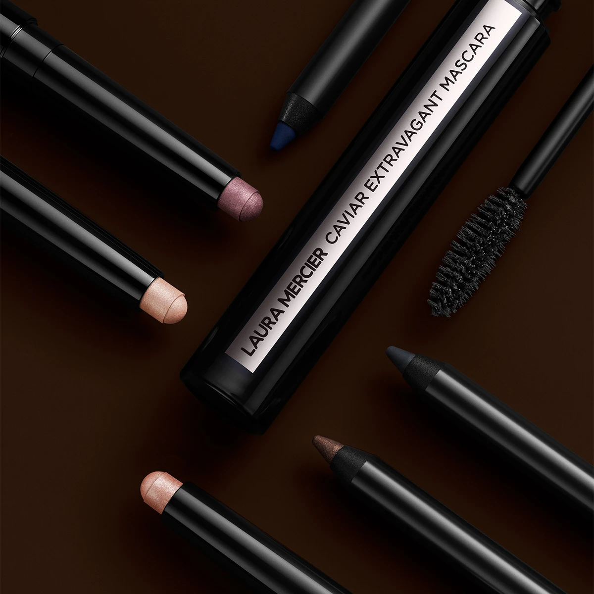 Laura Mercierin Caviar Extravagant Mascara, jota ympäröivät erilaiset silmämeikin tuotteet, mukaan lukien silmänympärys- ja silmänympärysvarjostimet lyijykynän muodossa, tummalla pohjalla.