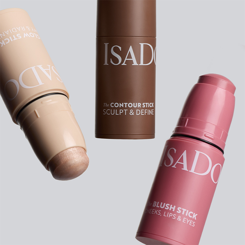 Tre IsaDora makeupstifter i ulike nyanser med teksten The Contour Stick Sculpt & Define og The Blush Stick Cheeks, Lips & Eyes mot lys bakgrunn. Produkter for contouring og blush i kremformat.