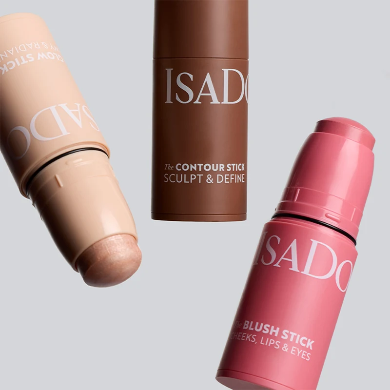Tre IsaDora makeupsticks i olika nyanser med texten The Contour Stick Sculpt & Define och The Blush Stick Cheeks, Lips & Eyes mot ljus bakgrund. Produkter för contouring och rouge i krämformat.