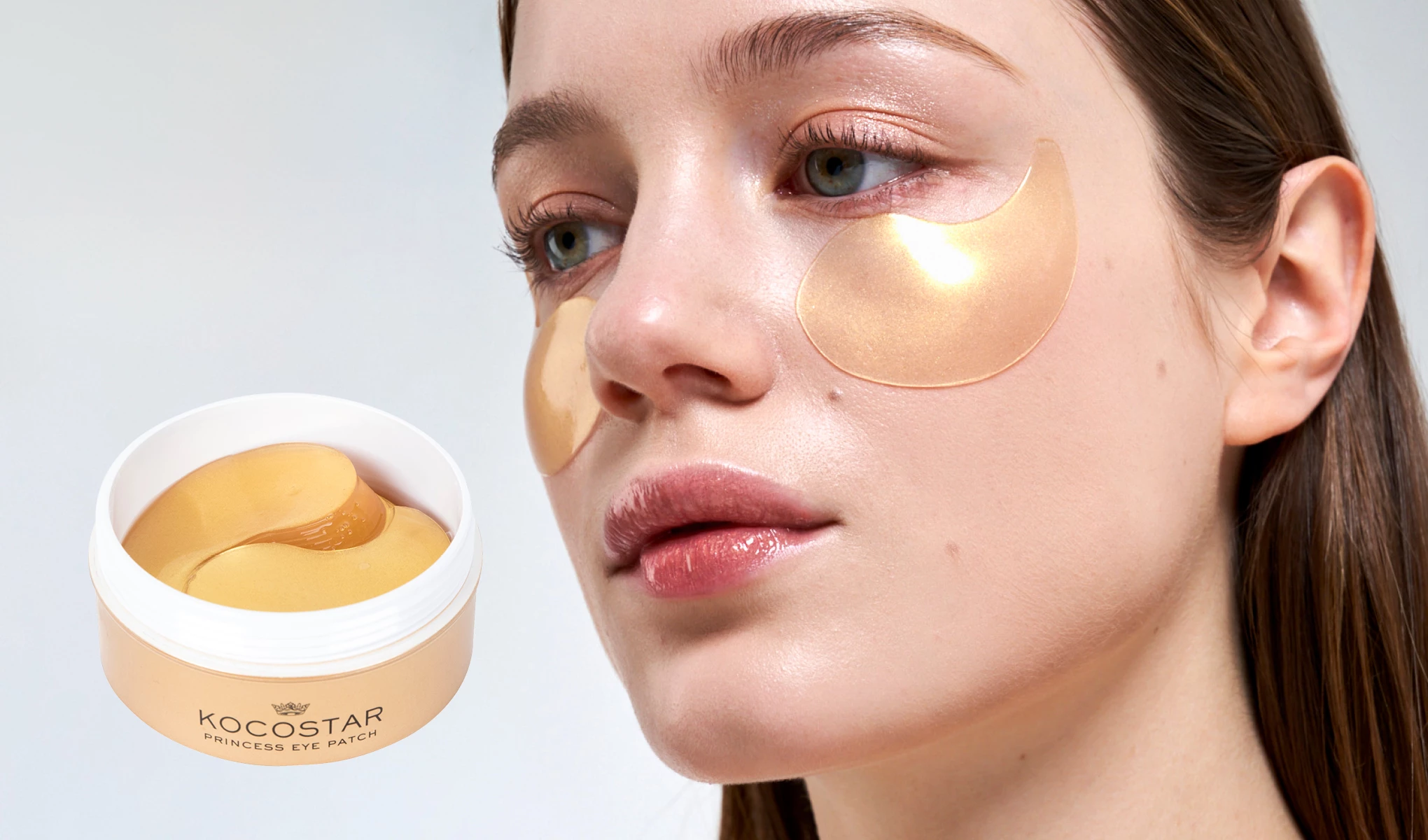 En krukke med Kocostar Princess Eye Patch, gylne øyemasker, plassert ved siden av en person med brunt hår og lys bakgrunn.
