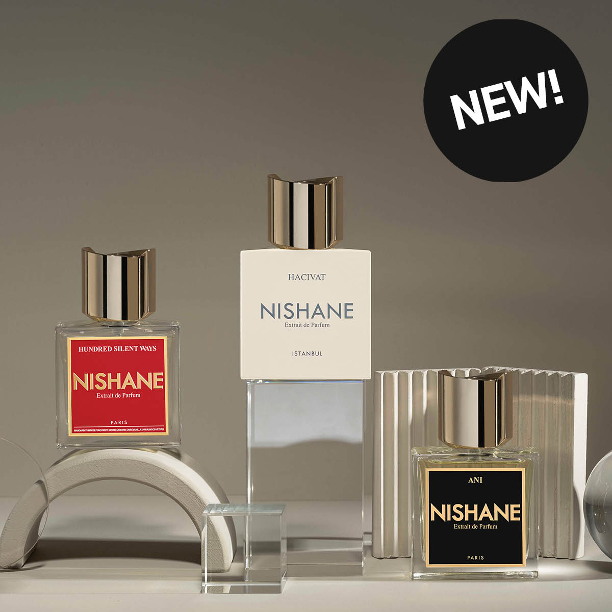 Tre Nishane-parfymer står utstilt på et bord. Den til venstre med rød etikett, den i midten med hvit etikett og den til høyre med svart etikett. Flaskene har elegante, gylne korker og er omgitt av geometriske dekorasjoner.