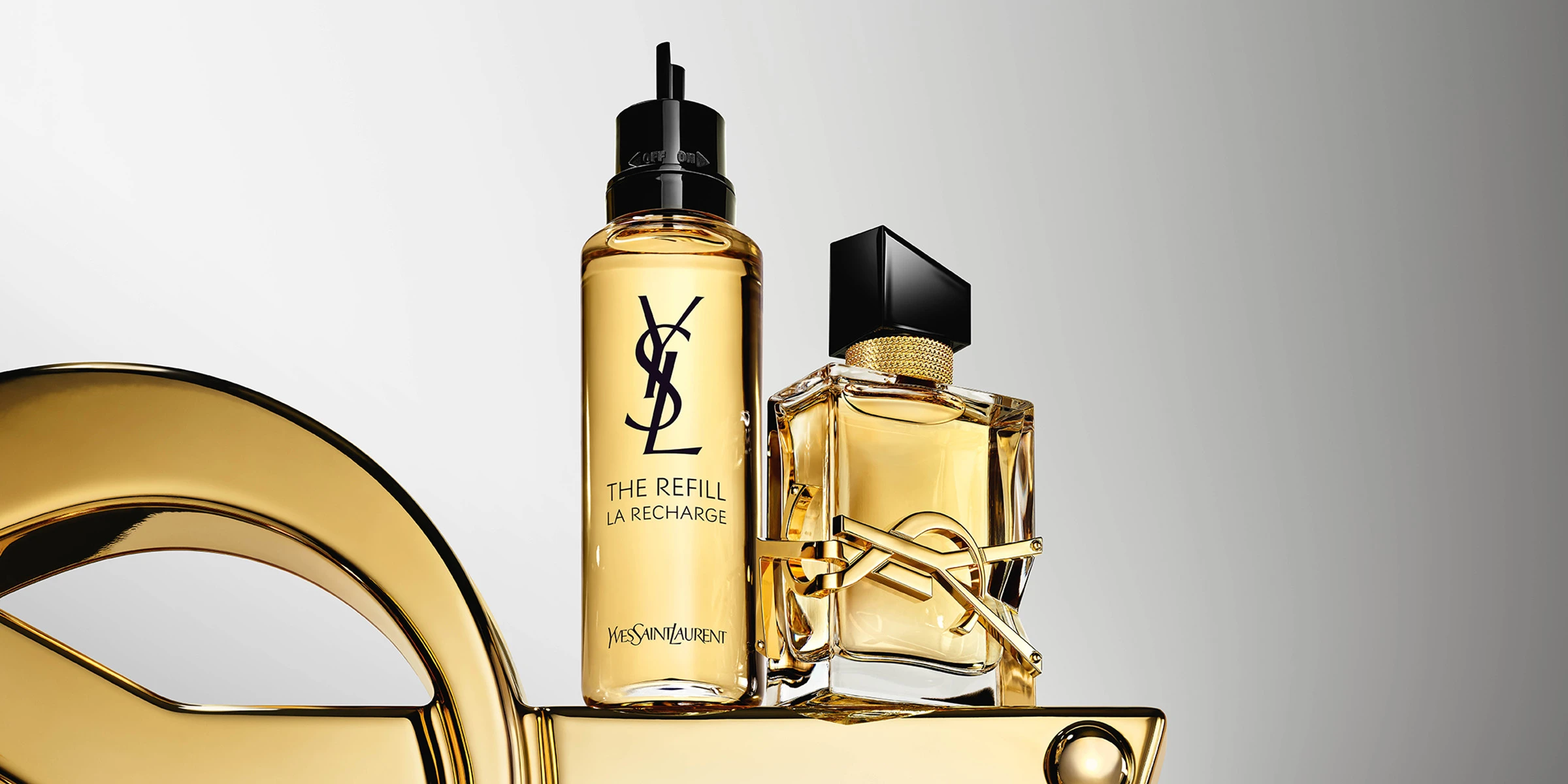 Yves Saint Laurent Libre Eau de Parfum -tuoksupullo ja täyttöpullo kultaisessa designissa vaaleaa taustaa vasten.