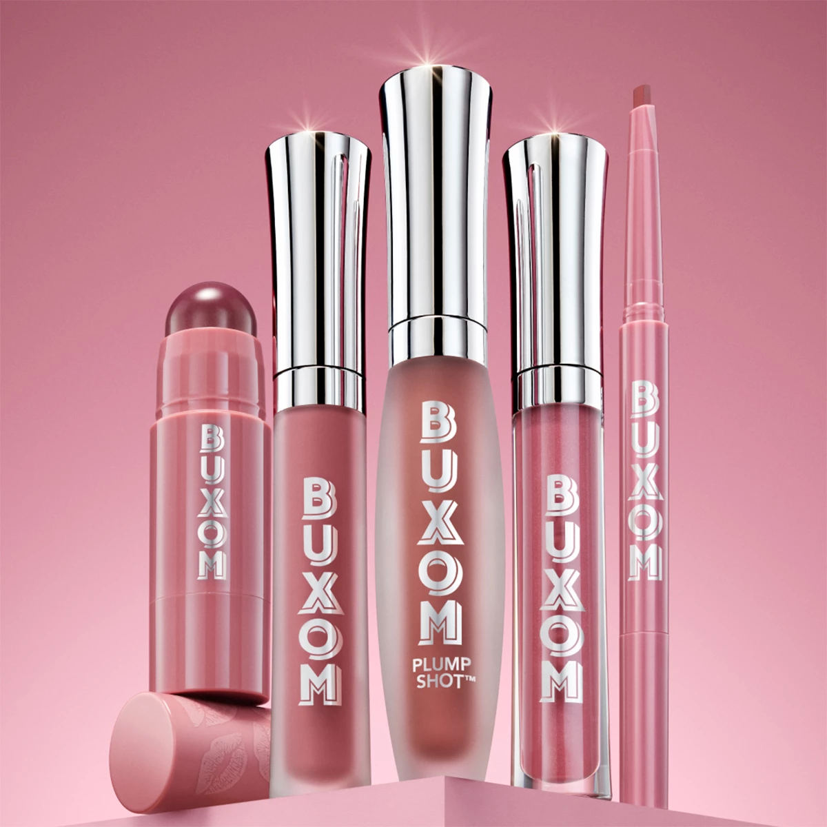 Fem Buxom-leppeprodukter i forskjellige rosa nyanser, inkludert leppestift, lipgloss og leppeblyant, arrangert på en rosa bakgrunn.
