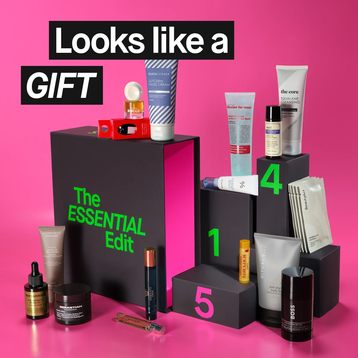 Kokoelma monipuolisia hoitotuotteita "The ESSENTIAL Edit" -sarjasta, sisältäen ihonhoito- ja tuoksutuotteita, järjestettynä mustille laatikoille pinkkiä taustaa vasten. Teksti: "Looks like a GIFT".